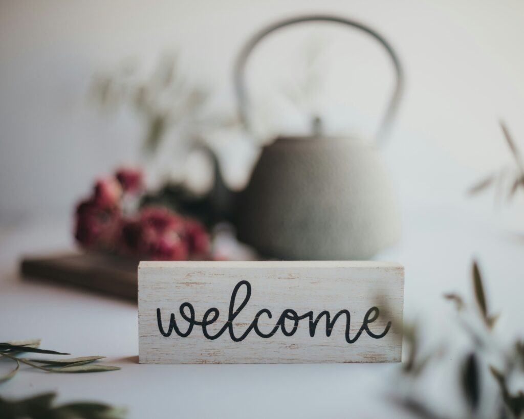 Sign saying 'welcome' in front of a pot of tea and flowers